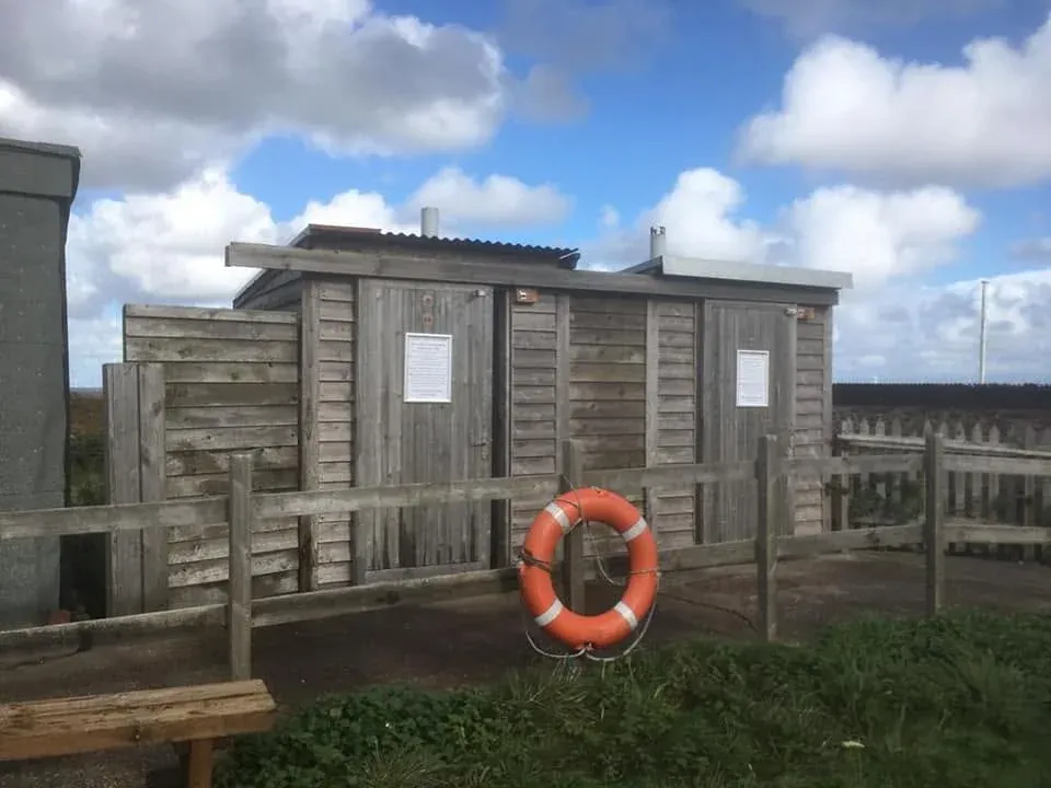 Timber-clad composting toilets on Hilbre Island with an orange lifebuoy in front